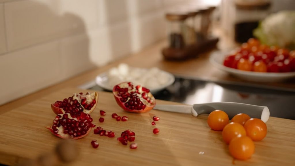 Aesthetic composition of pomegranate seeds and orange cherry tomatoes on a wooden board.